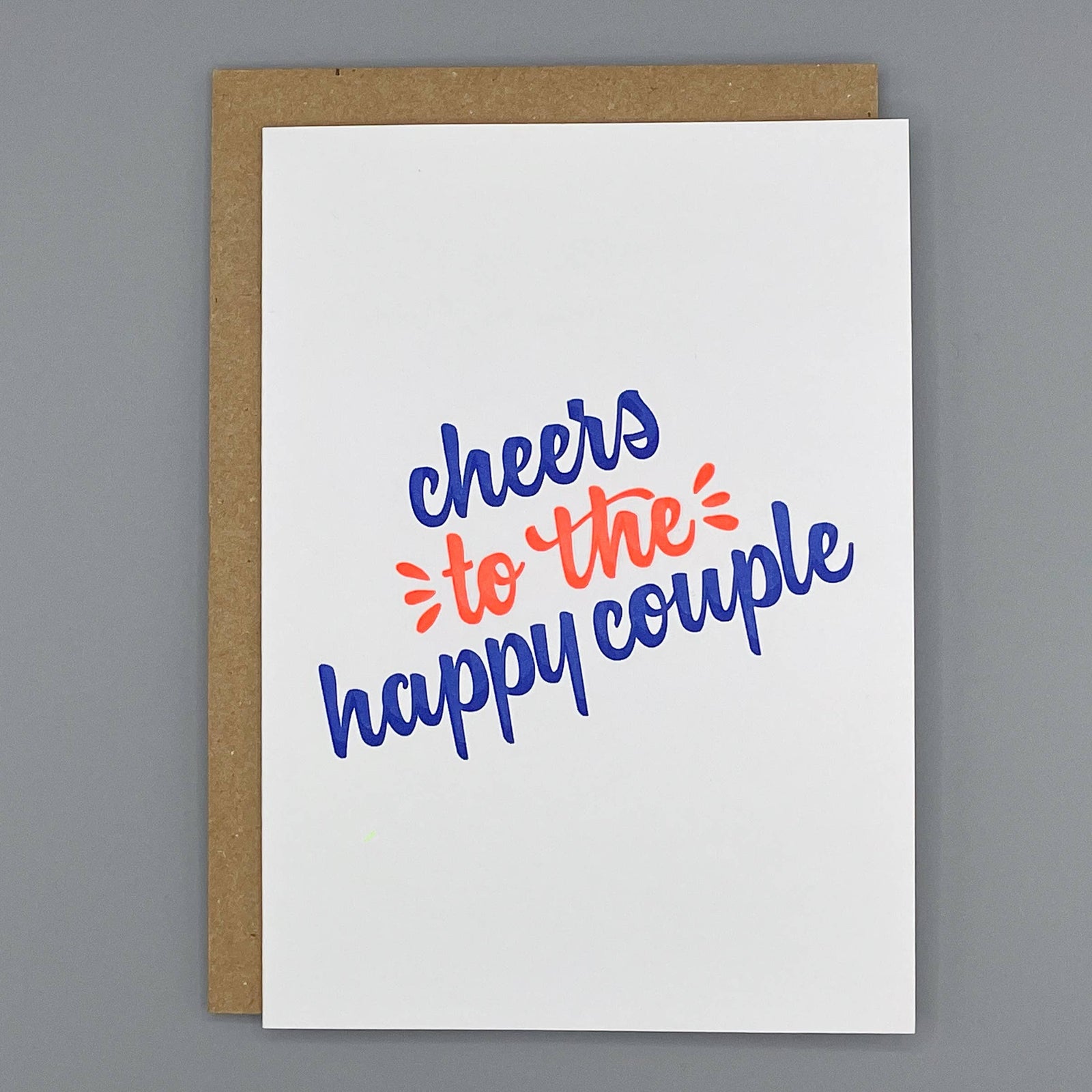 Letterpress congratulatory card with 'cheers to the happy couple' text on a cream background