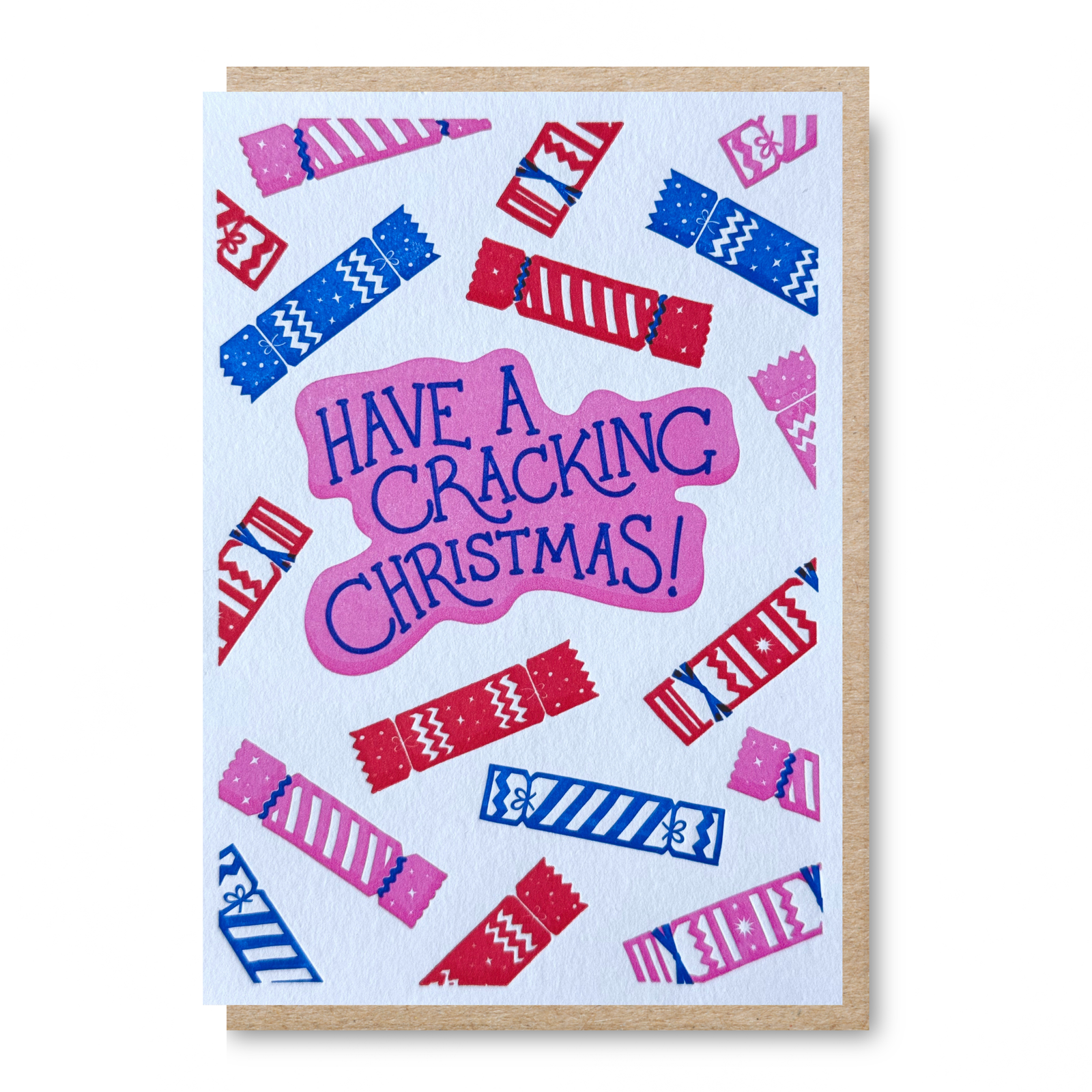 A Christmas greeting card with a kraft envelope, featuring the phrase 'HAVE A CRACKING CHRISTMAS!' in blue lettering on a pink shape, surrounded by illustrated red and blue crackers on a white background.