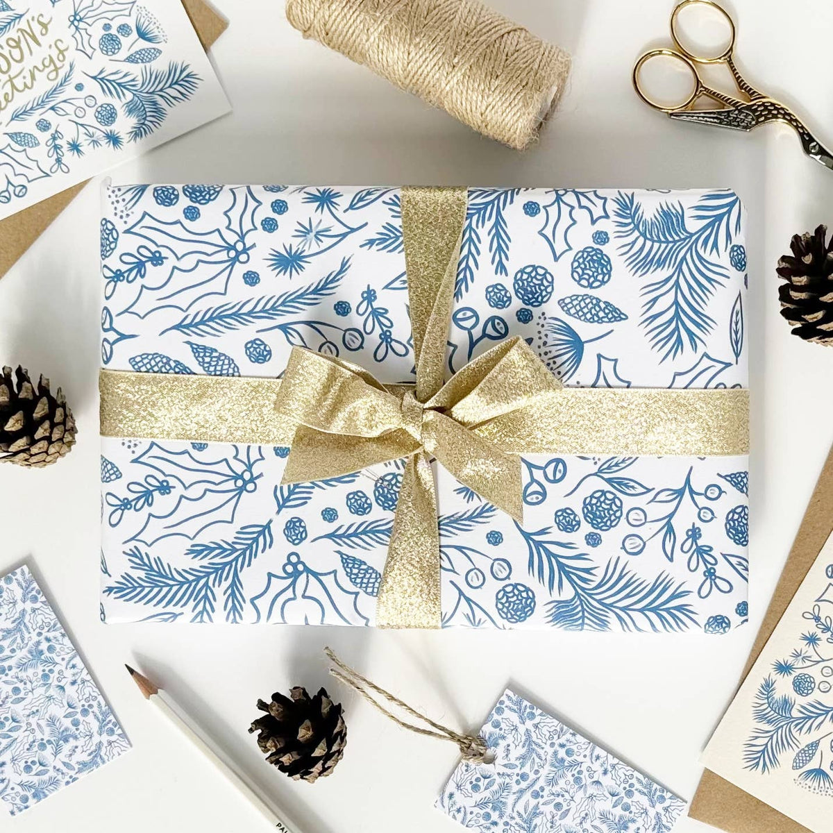 Gift wrapped present in blue and white patterned paper with a gold ribbon, surrounded by gift wrapping supplies on a white surface.