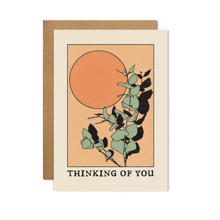 A greetings card with a black frame around the side and an image of an orange sun in the background and a sage green eucalyptus in the foreground. The words 'thinking of you' feature in black at the bottom.