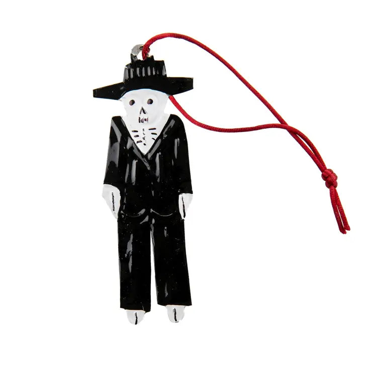 An image of a handmade tin decoration in the shape of a white skeleton in a black suit and hat. The tin decoration has a red hanging loop attached.