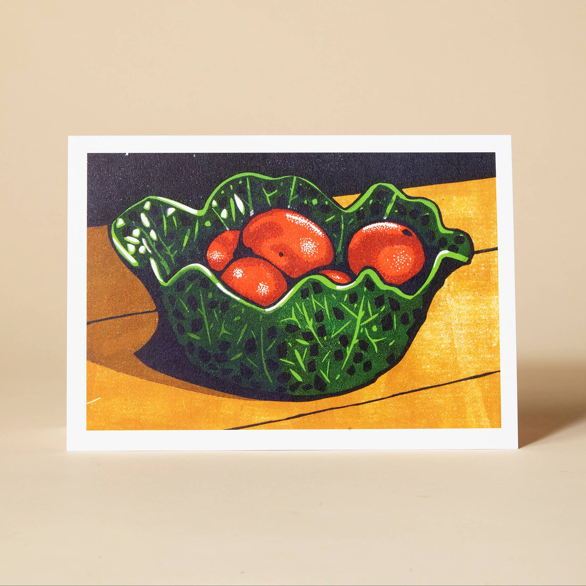 A greetings card featuring a colourful still life painting of three red-orange satsumas in a textured green bowl, displayed on a beige surface against a light beige background.