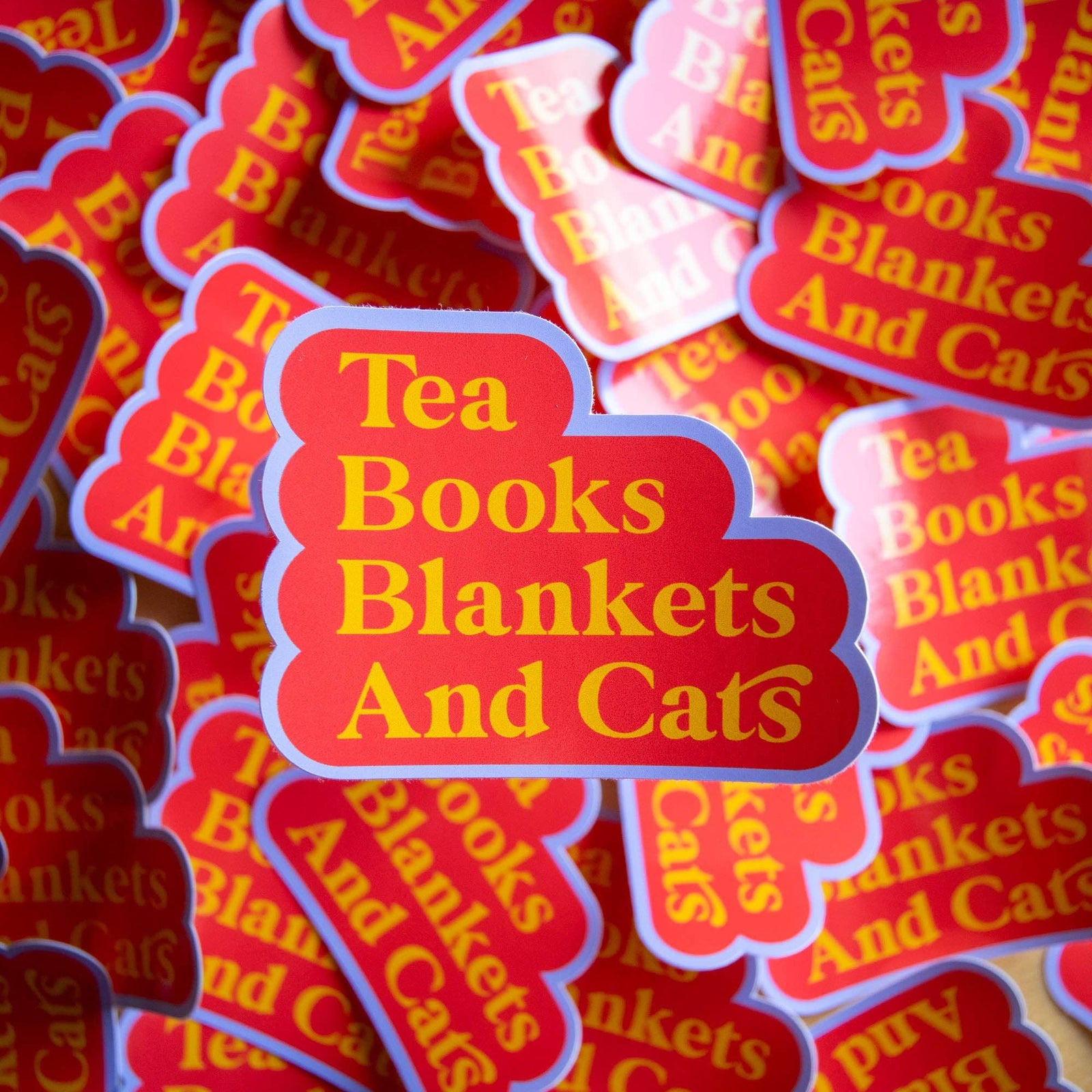 Stack of red and yellow 'Tea Books Blankets And Cats' stickers.