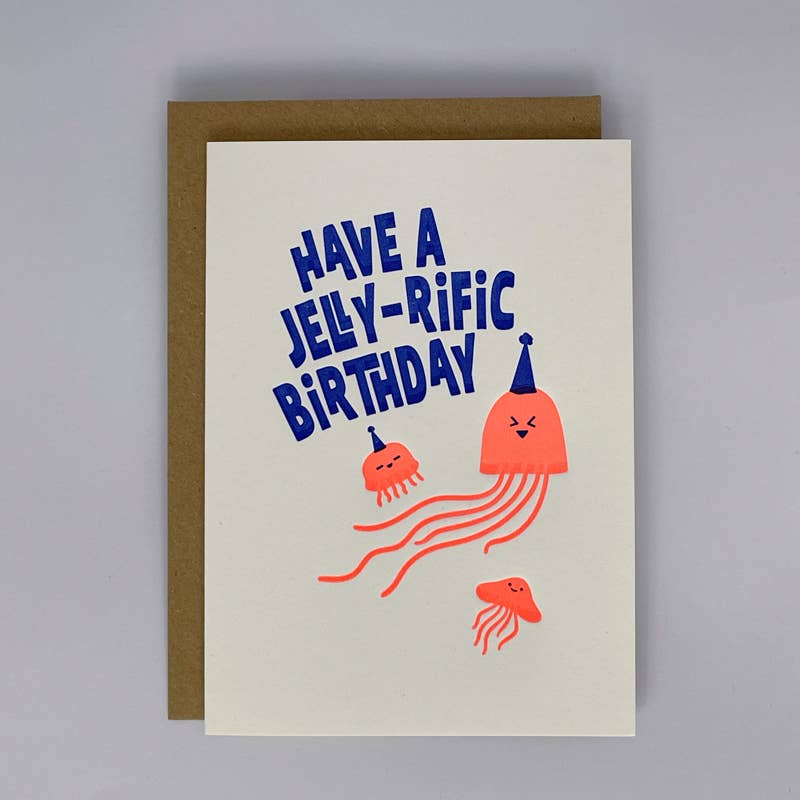 A birthday card with a brown envelope, featuring the text 'HAVE A JELLY-RIFIC BIRTHDAY' in blue, above three orange jellyfish illustrations on an off-white card background.