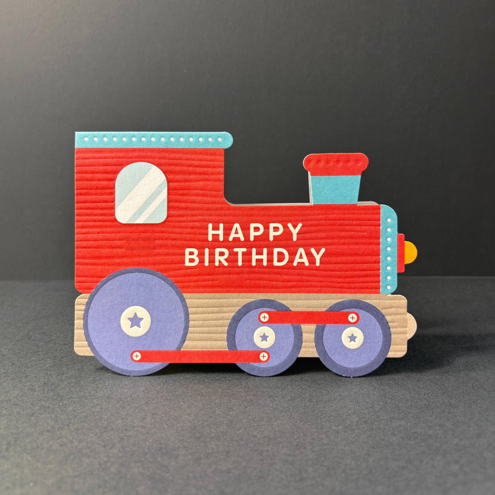 Red toy train cut out birthday card with 'Happy Birthday' text on a dark background by Heyyy cards at penny black