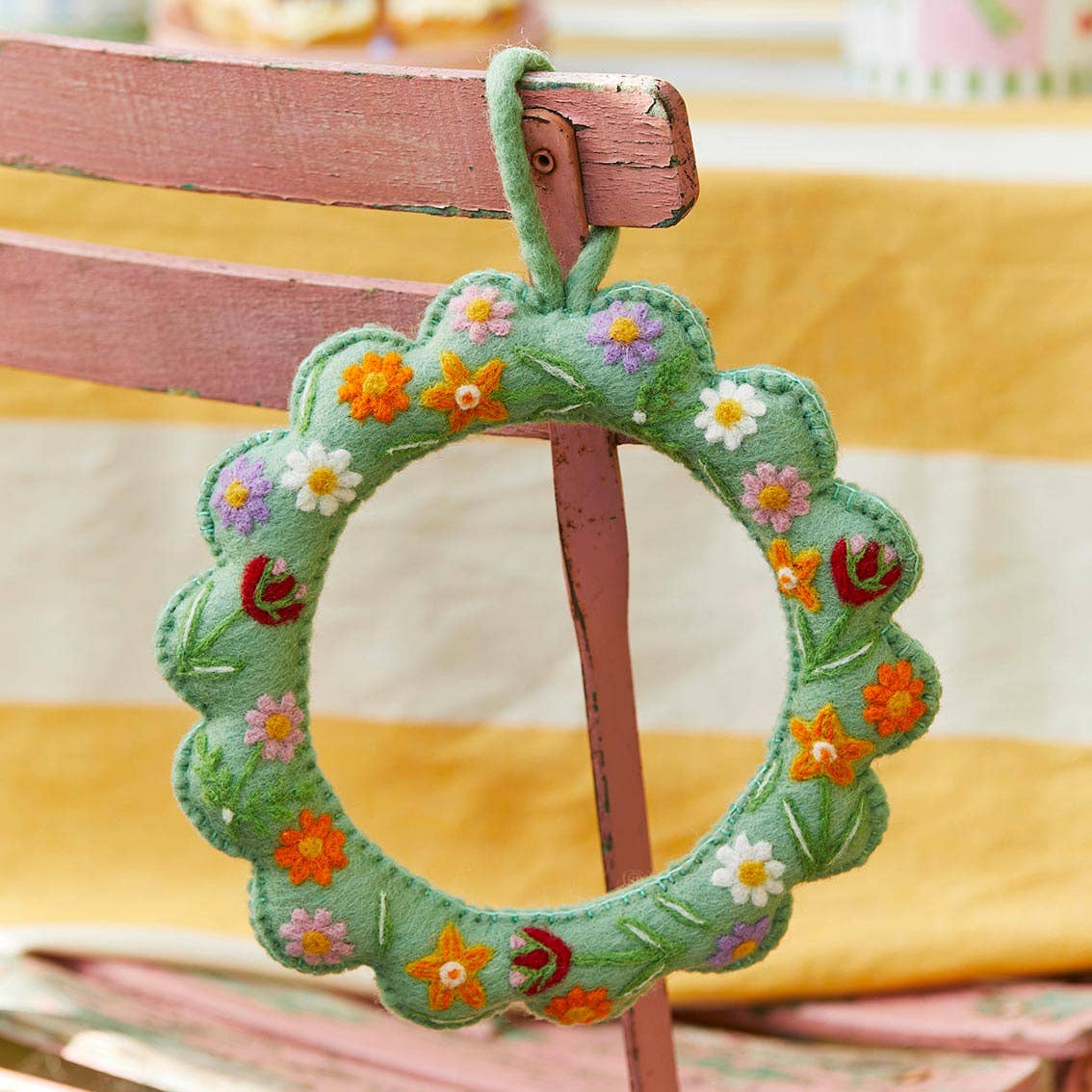 Floral Scalloped Felt Spring Wreath by penny black shown hanging on a chair at a party