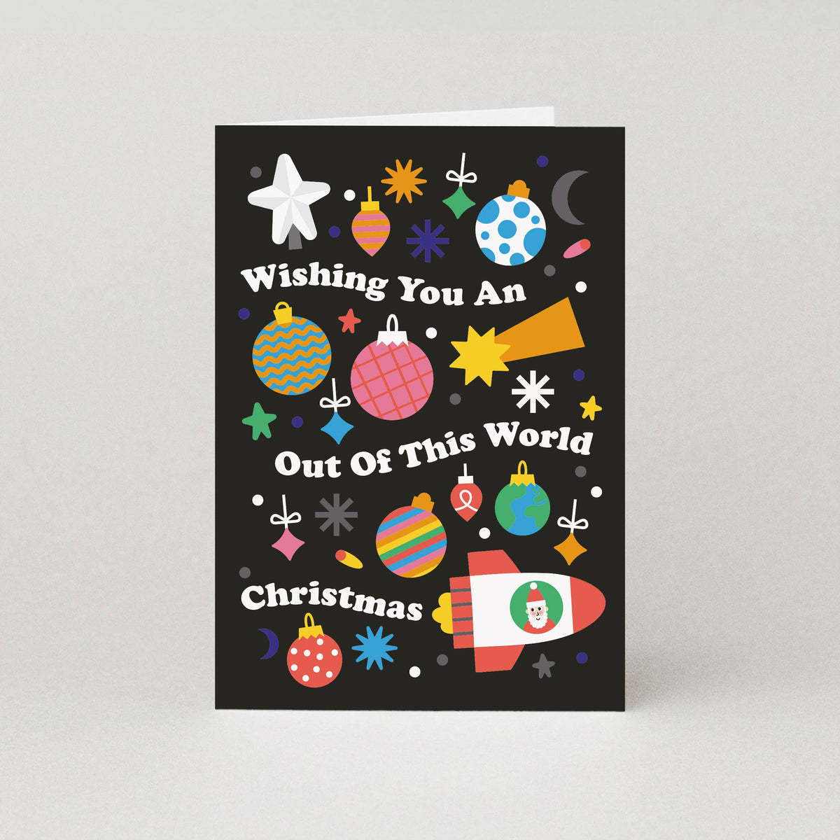 A Christmas greeting card with a black background and colourful festive illustrations, including ornaments, stars, snowflakes, a crescent moon, and a rocket ship. The text on the card reads, 'Wishing You An Out Of This World Christmas'.