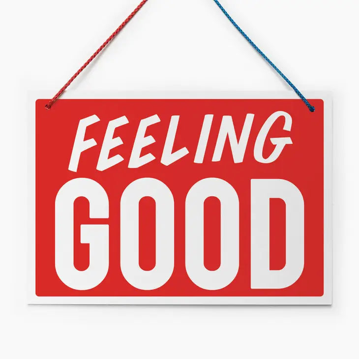 An image of a red hanging sign with a vintage feel. It has the words &#39;Feeling Good&#39; in white block capitals and a half red/half blue hanging cord.
