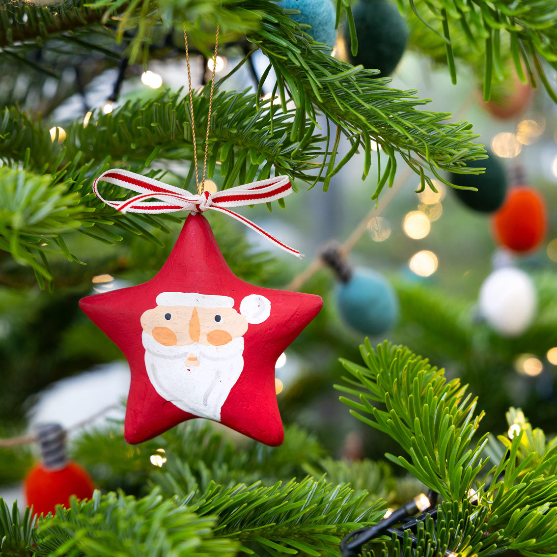 Red star-shaped Christmas ornament with Santa Claus face hanging on a christmas tree by talking tables at penny black