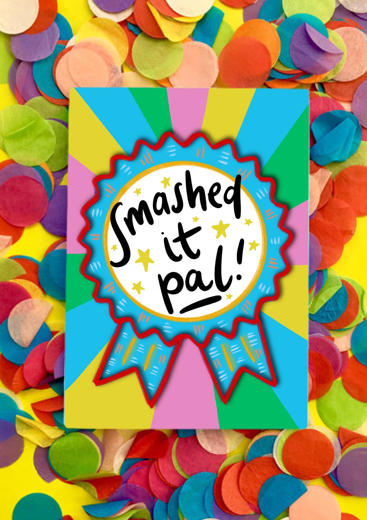 A greetings card with a rainbow sunbeam designed background with a large rosette motif. The rosette is light blue with red edging and has a large white circle in the middle that has the words handwritten &#39;smashed it pal&#39;. The card is lying on a bed of rainbow confetti.