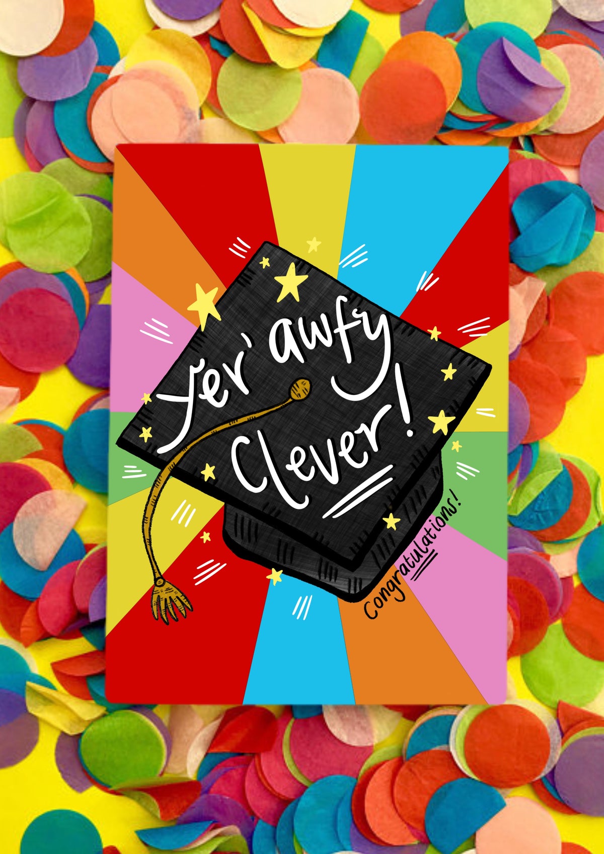 A greetings card with a rainbow sunbeam background and a black graduation cap in the middle. It has a gold tassel and white script writing saying &#39;yer awfy clever&#39;! Underneath is also says &#39;congratulations&#39;. The card is lying on a bed of rainbow confetti.