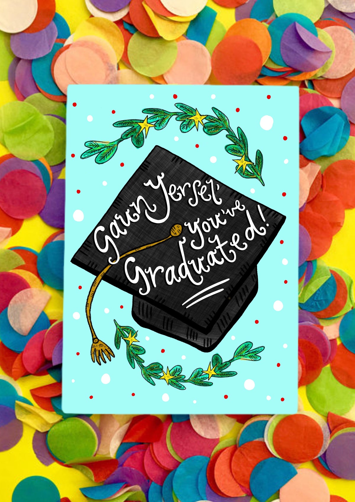 A greetings card wiht a light turquoise background and a large graduation black cap in the middle with gold tassel. In white writing, it says on the cap &#39;Gaun Yersel&#39; you&#39;ve graduated!&#39; in script handwriting. There are leafy branches at the bottom and top of the card also. The card is sitting on a bed of rainbow confetti.