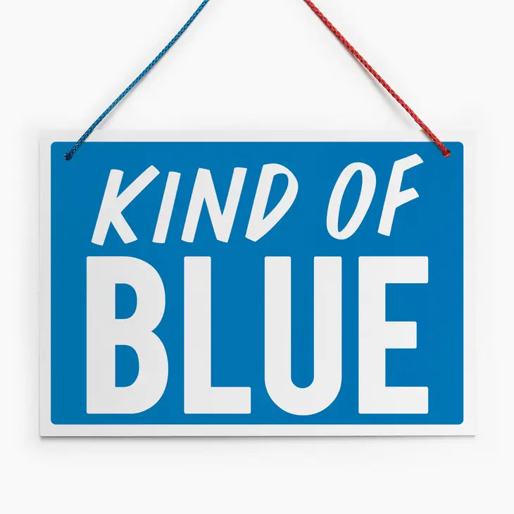 An image of a blue hanging sign with a vintage feel. It has the words &#39;Kind of Blue&#39; in white block capitals and a half red/half blue hanging cord.