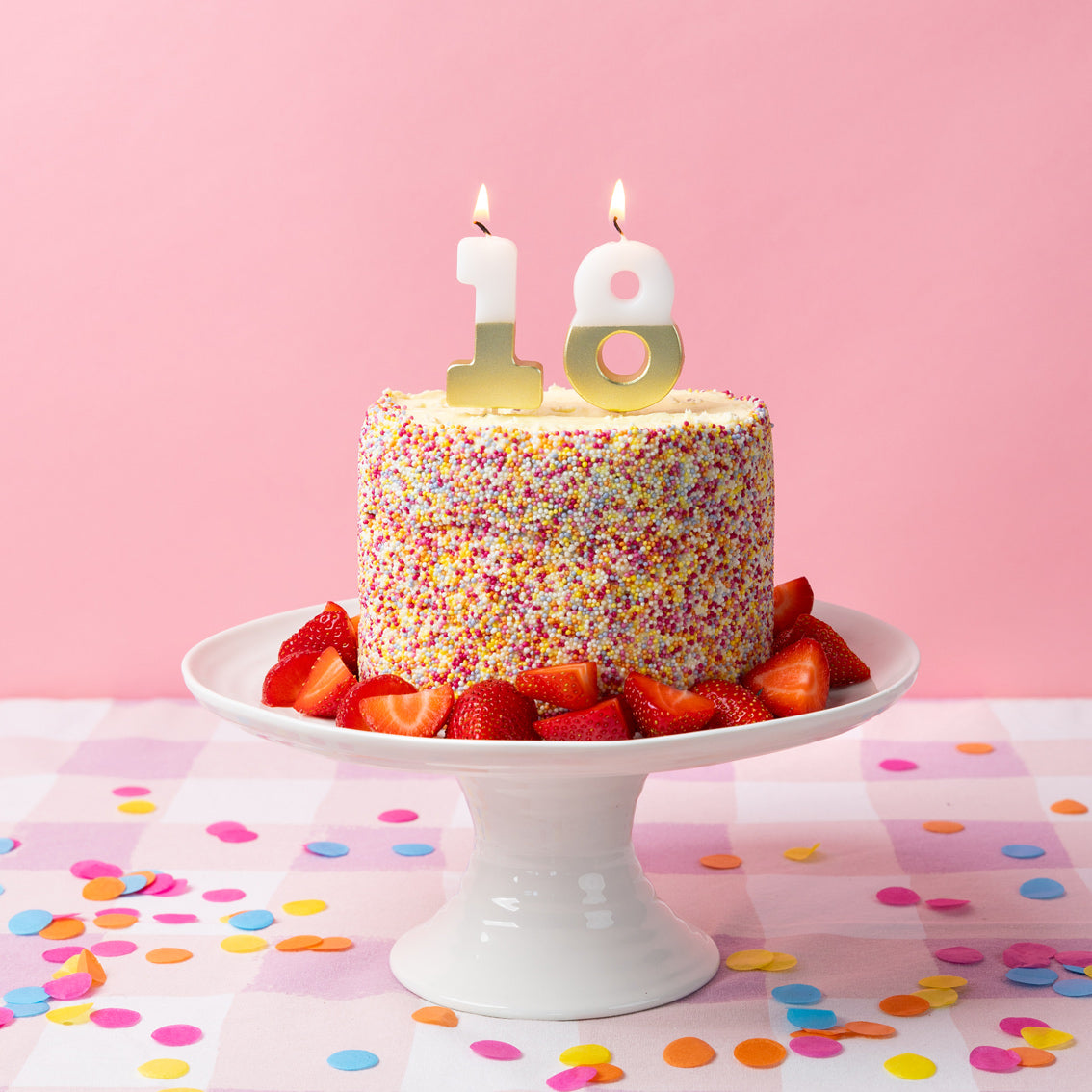 White &amp; Gold Number Milestone Birthday Candle 18 set on top of a cake covered in sprinkles