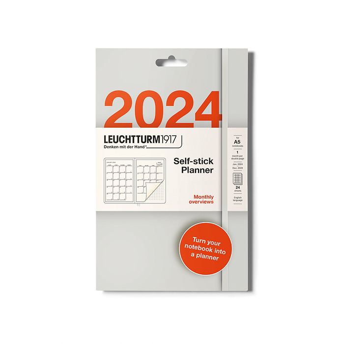 Retail packaging in grey and white for self-stick planner stickers by brand Leuchtturm1917. It shows the month grid over two A5 pages in a small illustration and that it&#39;s for the year 2024. It also has an orange circle towards the bottom and in white writing it says &#39;turn your ntoebook into a planner&#39;.