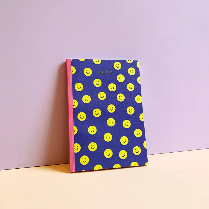 An image of a dark blue notebook covered in yellow circle happy faces, with a pink spine.