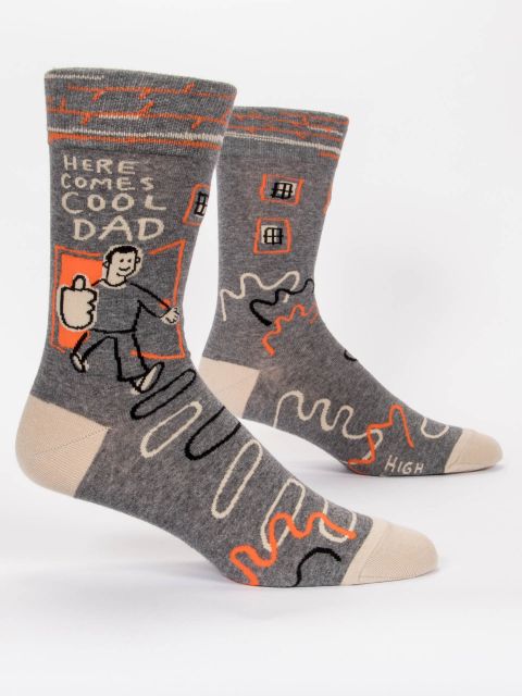 A pair of grey socks with black, white and orange squigly lines. The image is a white person walking through an orange door with an oversized thumbs up and the words 'Here Comes Cool Dad'
