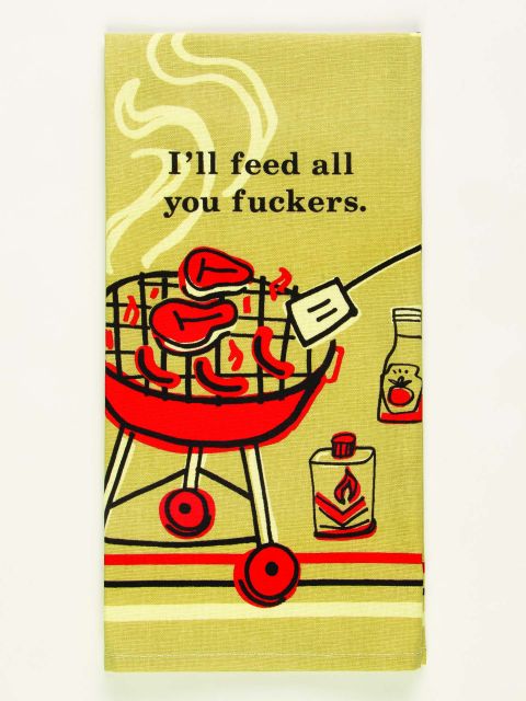 A folded beige tea towel showing the main design of a red barbeque cooking a variety of meat and someone about to flip something with a fish slice and the words in black above, 'I'll feed all your fuckers'.