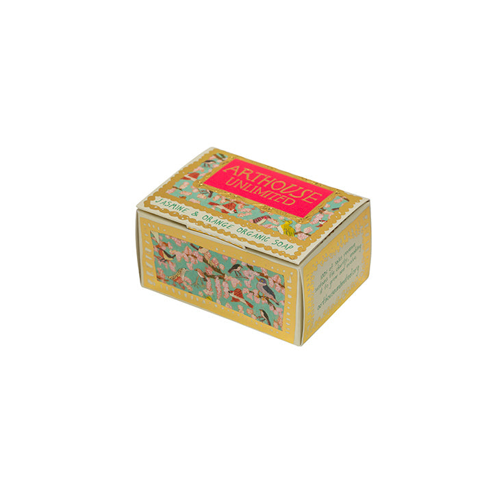 A cuboid shape box with guilded gold edging and a bright red/pink label stating the company Arthouse Unlimited. There is a background illustration of colourful birds. The box also states the words 'jasmine & orange organic soap'.