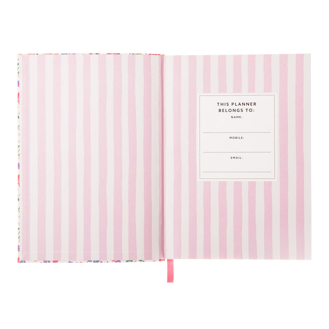 An image showing the first opened page of a planner. The design is light pink and white vertical stripes. The second page includes a boiler plate to include the owners name, mobile and email. A cerise pink page marker ribbon is shown.