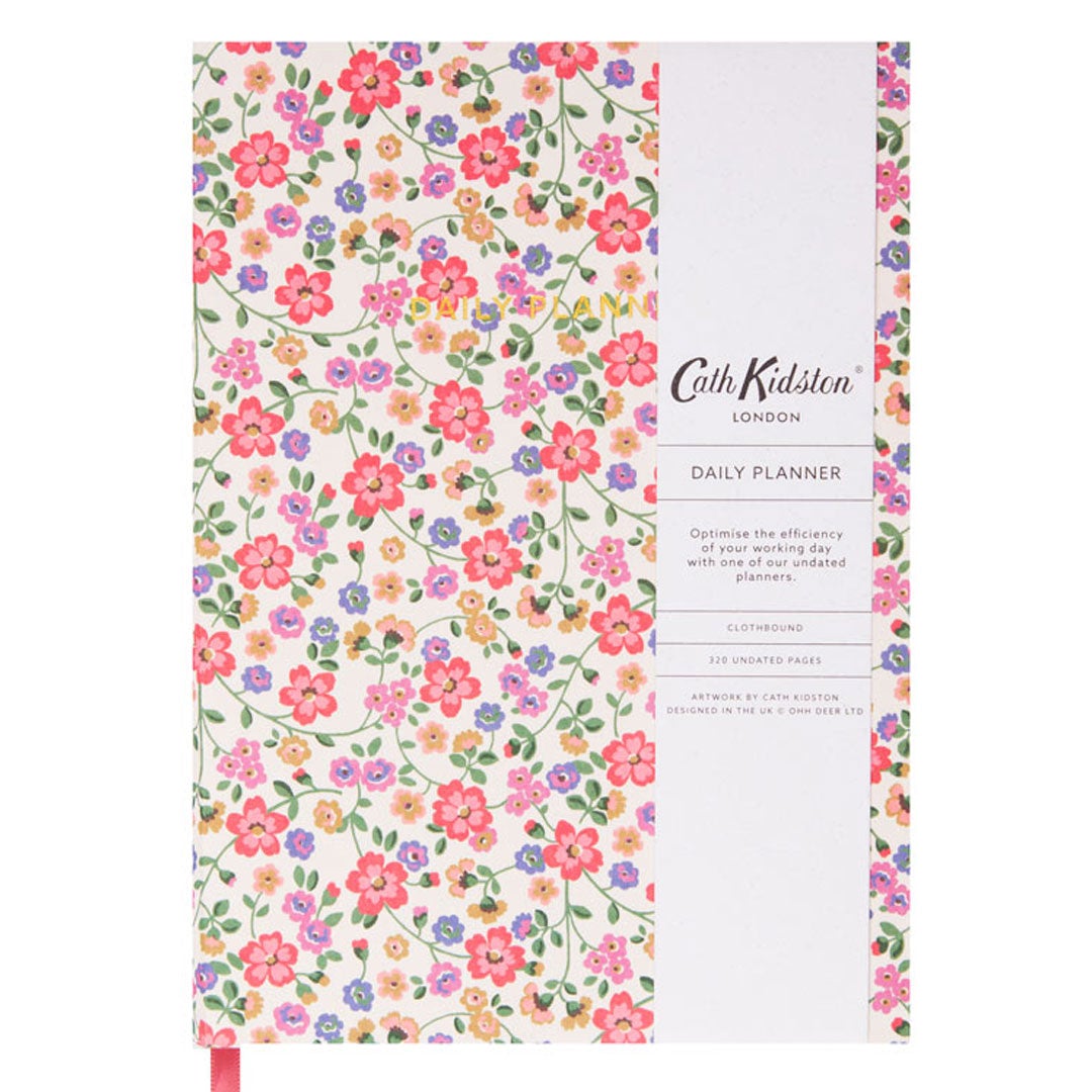 The front cover of a daily planner by Cath Kidston. The cover design has a cream background and is covered in pastel colour flowers in  pink, peach, yellow and lilac. There are gold embellished words saying in capitals 'DAILY PLANNER'. The image shows a white belly band including details about the product.