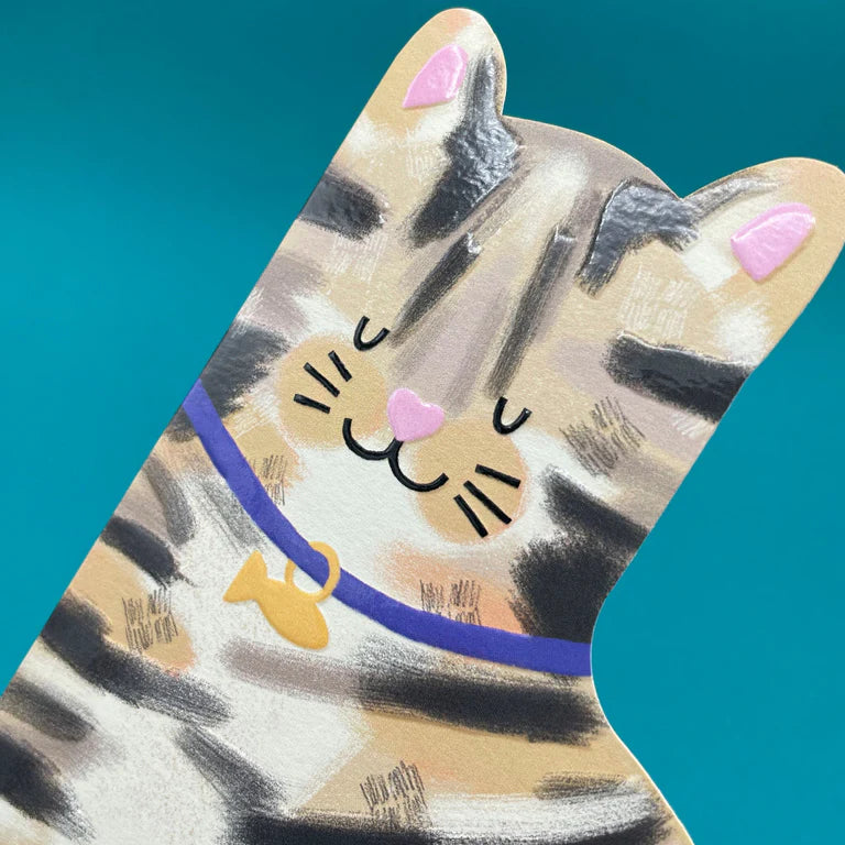 A card cut out in the shape of a brown and black striped tabby cat with it&#39;s eyes closed. The cat is sitting happily and has a fish shape attached to it&#39;s navy colour.