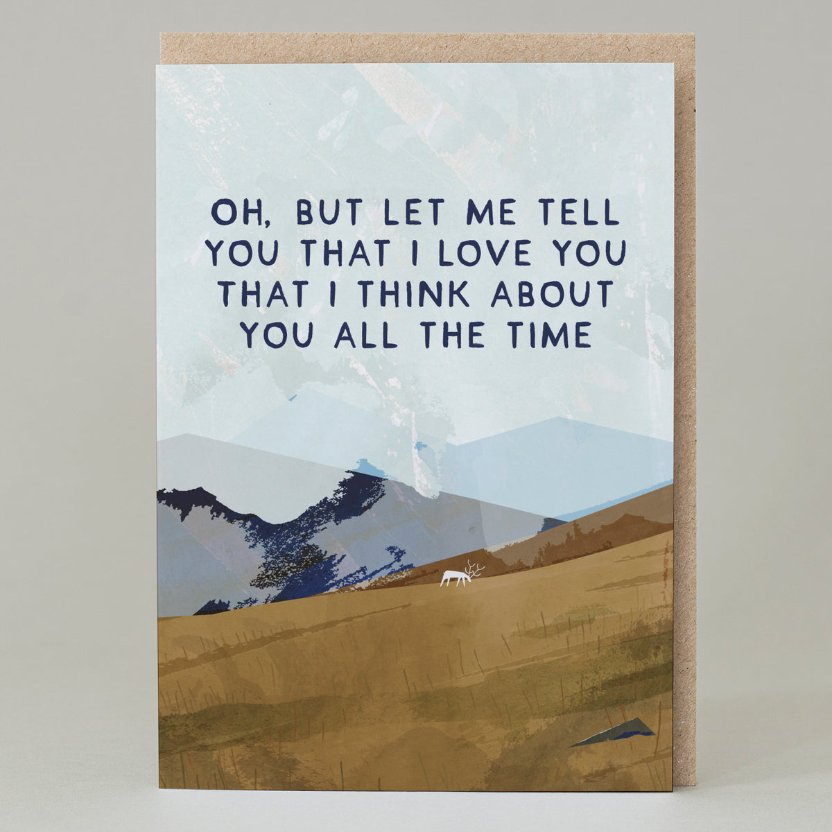 A greetings card featuing a sloping hillside with a white grazing deer and jagged mountains in the background. It uses earthy colours and features lyrics to the famous scottish song Caledonia in navy capital letters in the middle - Oh, But Let me tell you that I love you that I think about you all the time.