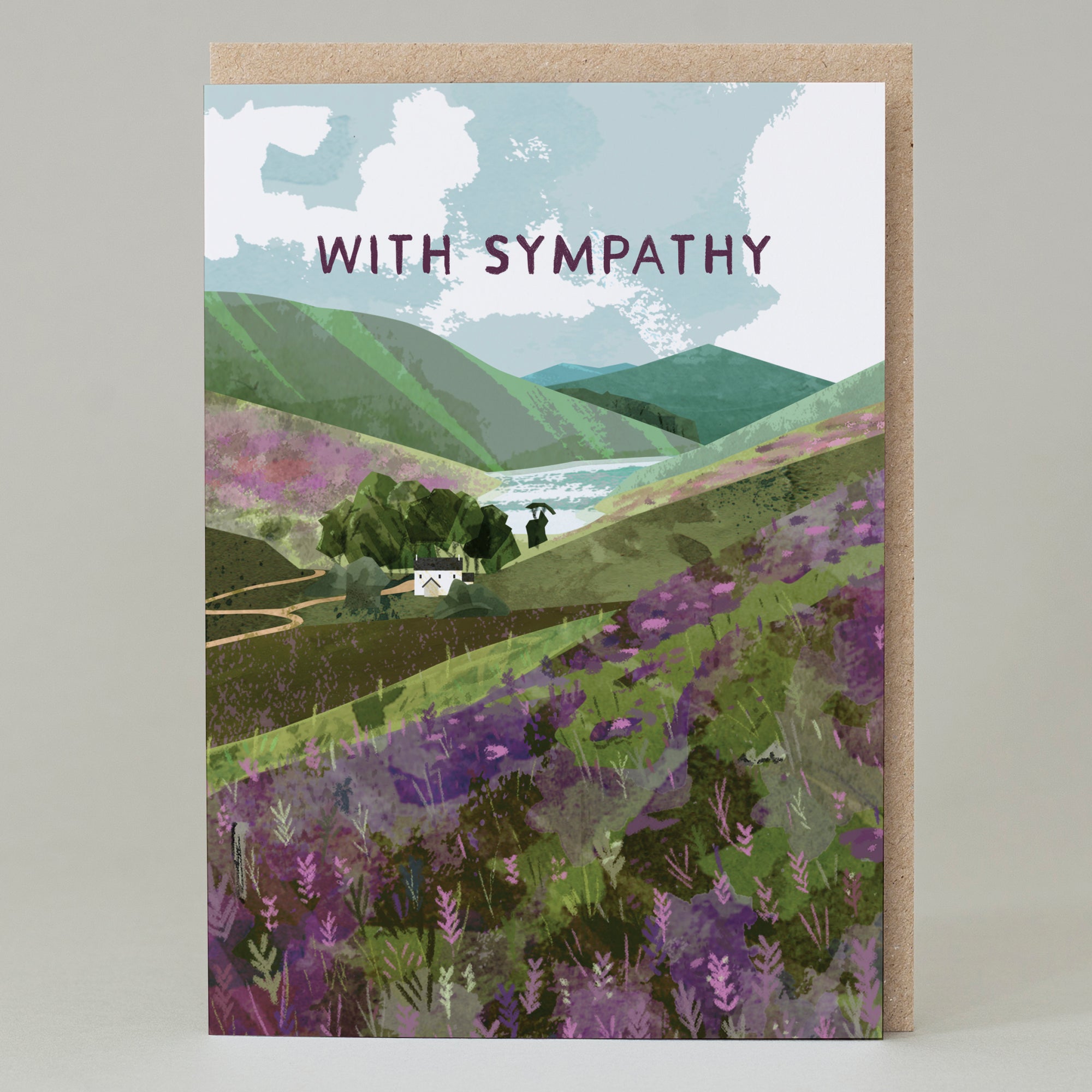 A greetings card featuring purple capital letters saying With Sympathy in the sky of a hilly landscape. There is purple heather on the hillsides, leading down to a track and a cottage overlooking a loch.